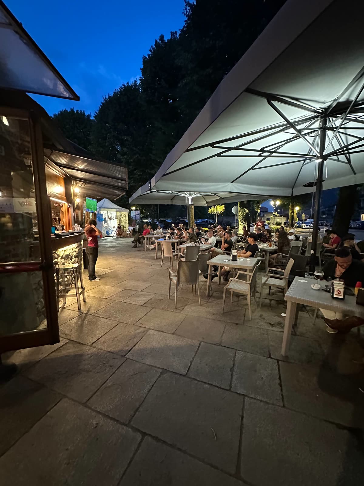 Il cortile del Cortiletto al blue hour, con i tavolini all'aperto animati e il bancone illuminato